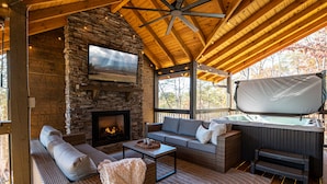 Un espacio al aire libre acogedor con chimenea de piedra, sofá y jacuzzi.