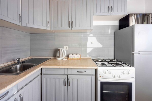 Una cocina con gabinetes grises, un lavamanos de acero inoxidable, una estufa a gas y un refrigerador blanco.