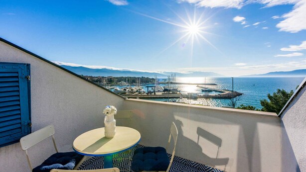 Ein Balkon mit Tisch und Stühlen mit Blick auf einen Hafen und das Meer.