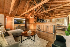 A spacious living area with a wooden ceiling, a television, a sofa, a coffee table, and a kitchen area with a bar.