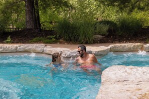 A swimming pool with clear blue water, surrounded by natural vegetation and stone walls. - Spacious Resort Cabin – Sleeps 16, Minutes to Silver Dollar City! (Branson)