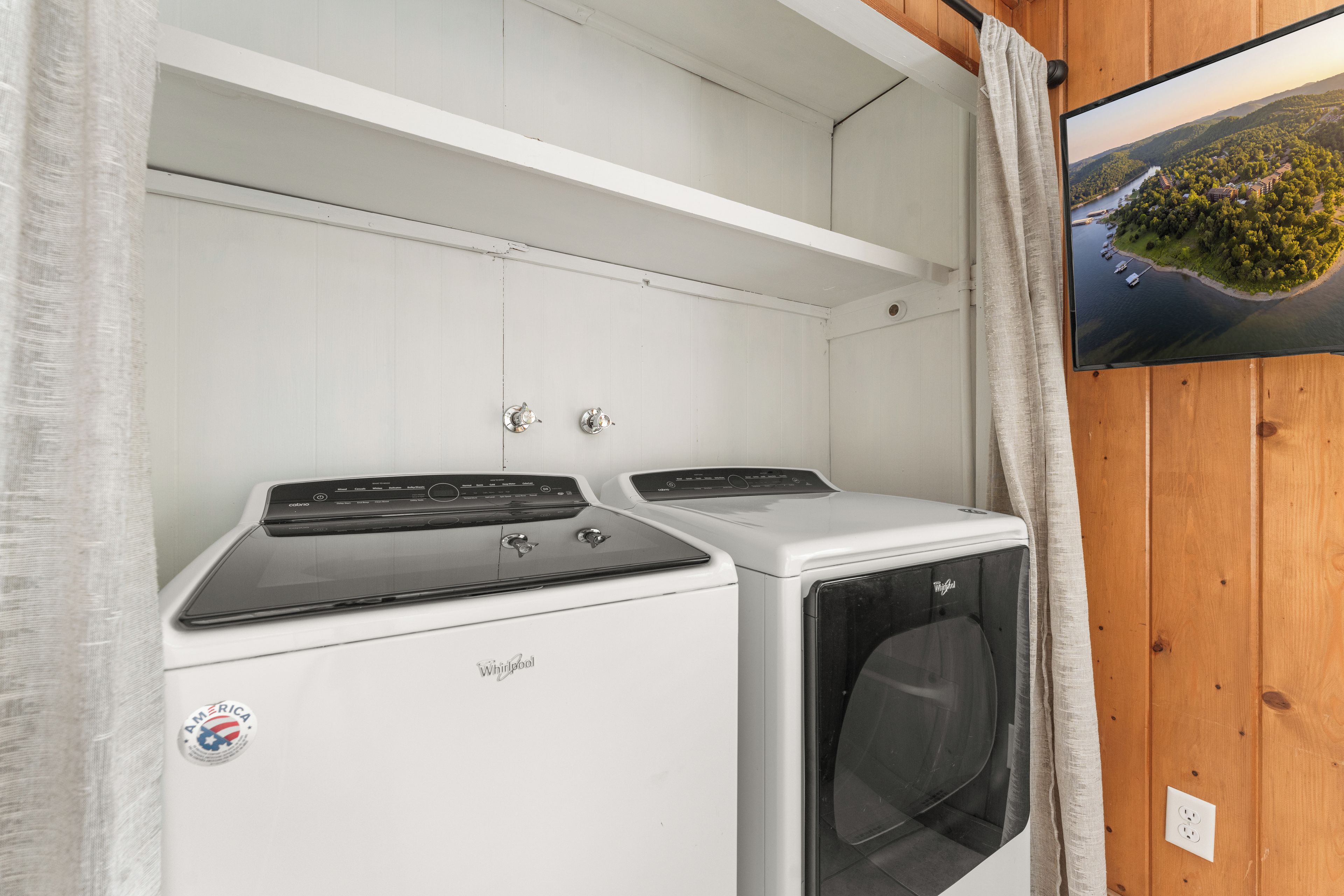 Ein Waschraum mit weißer Wand, einem wandmontierten Regal sowie einer Whirlpool Waschmaschine und einem Trockner.