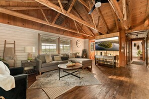 A cozy living room with a wooden ceiling, a sofa, a coffee table, and a television. - Spacious Resort Cabin – Sleeps 16, Minutes to Silver Dollar City! (Branson)