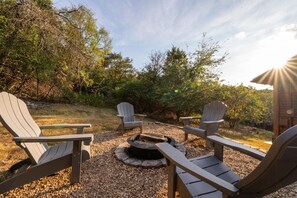 A patio area with four Adirondack chairs arranged around a circular fire pit.