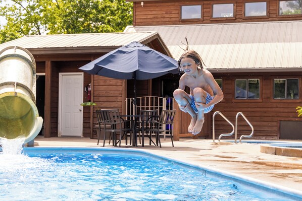 A swimming pool with a slide, a wooden deck, and a building with windows in the background.