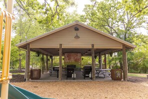 A covered picnic area with tables and barbecue grills, surrounded by trees.