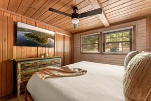 A wooden cabin room with a bed, a television on the wall, and a window with blinds. - Spacious Resort Cabin – Sleeps 16, Minutes to Silver Dollar City! (Branson)