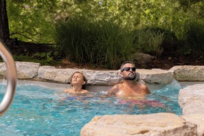 A hot tub with two people, surrounded by greenery. - Spacious Resort Cabin – Sleeps 16, Minutes to Silver Dollar City! (Branson)