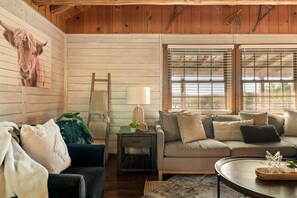 A cozy living room with a wooden ceiling, a sofa set, a coffee table, and a painting of a horse's head on the wall.