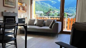 A modern living room with a sofa, chairs, and a dining table. A large window offers a view of a mountainous landscape. - Recently refurbished modern apartment with unhindered views of the Matterhorn. (Zermatt)