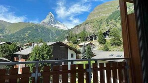 A mountain view with a prominent peak, surrounded by residential buildings and greenery. - Recently refurbished modern apartment with unhindered views of the Matterhorn. (Zermatt)
