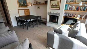 A modern living room with a sofa, a dining table with chairs, a fireplace, and a bookshelf. - Recently refurbished modern apartment with unhindered views of the Matterhorn. (Zermatt)