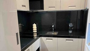 A compact kitchen with white cabinets, a black countertop, and a stainless steel sink. - Recently refurbished modern apartment with unhindered views of the Matterhorn. (Zermatt)
