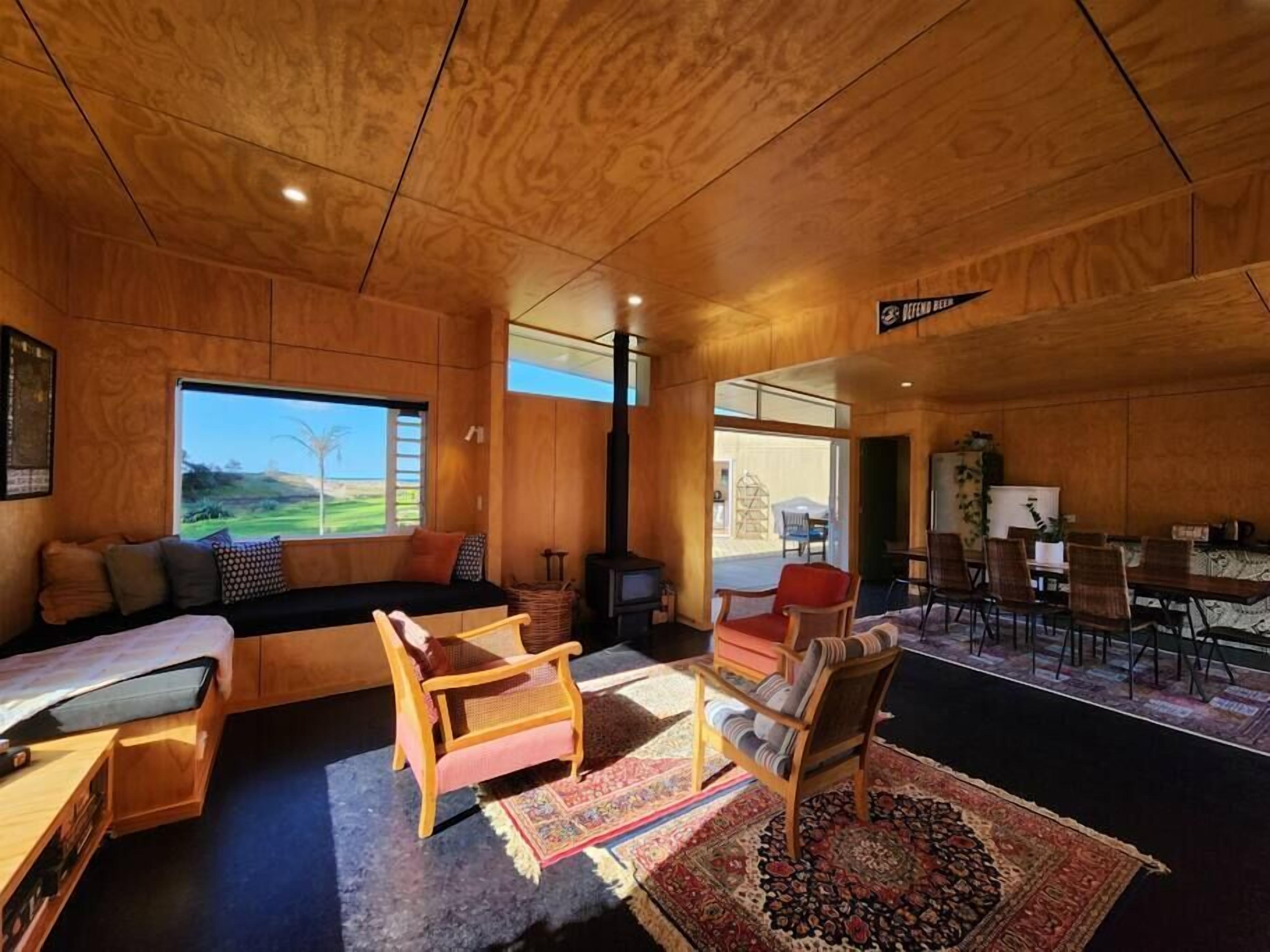 A cozy wooden interior with a sofa, chairs, a dining area, and a large window offering a view of the outdoors.