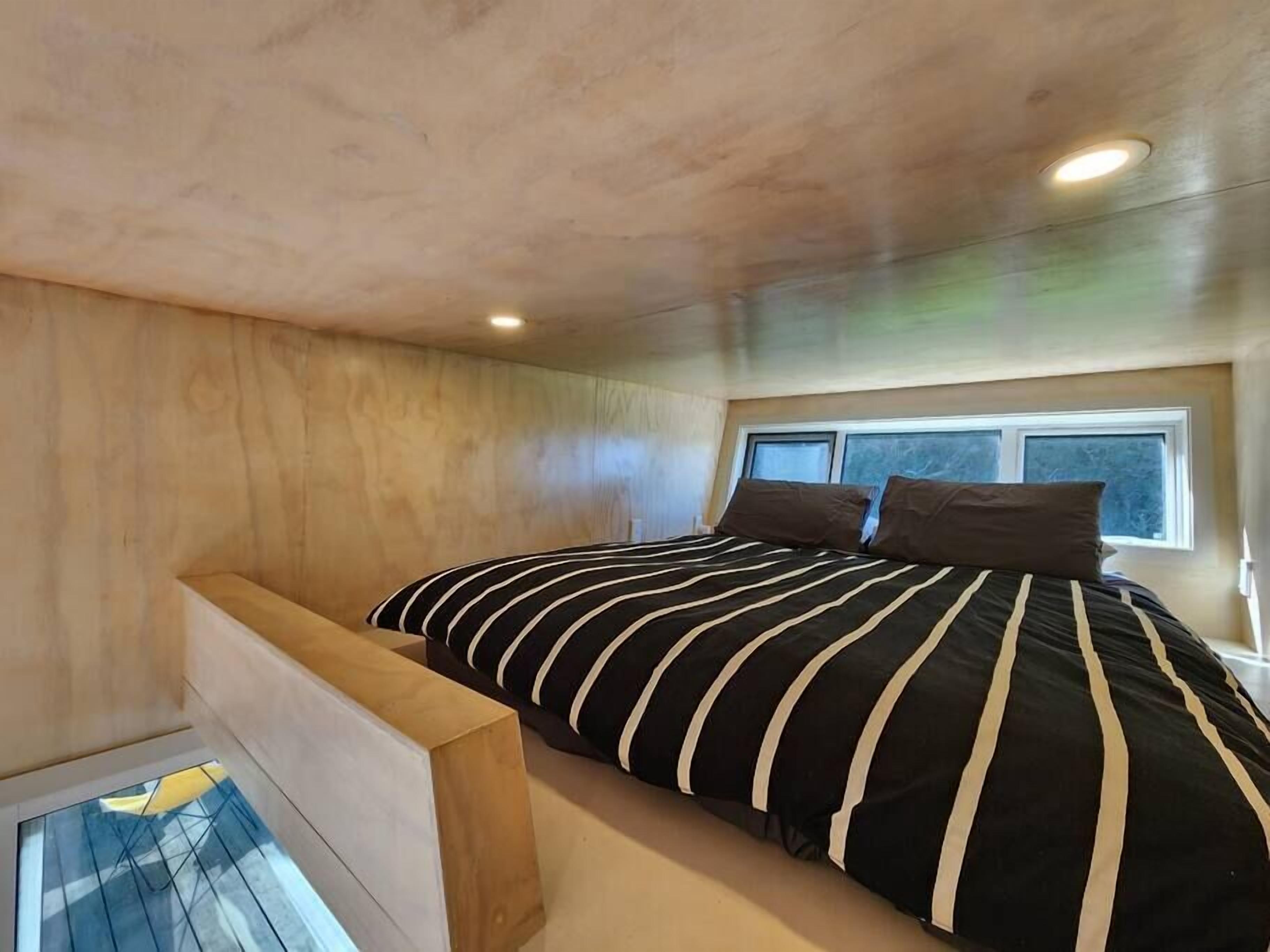 A bedroom with a sloped ceiling, a bed with striped bedding, and a window providing natural light.