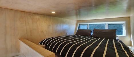 A bedroom with a sloped ceiling, a bed with striped bedding, and a window providing natural light.