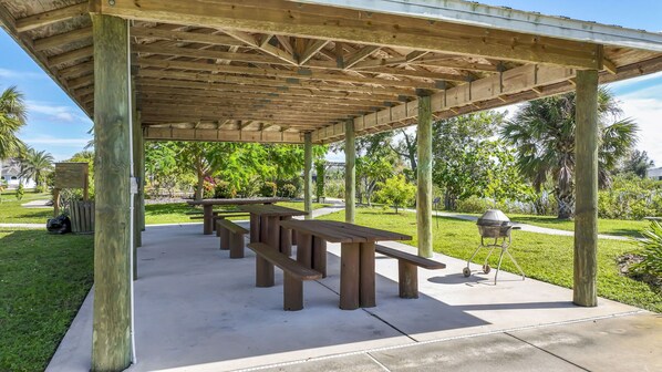 Un área de picnic techada con bancos de madera y una parrilla.