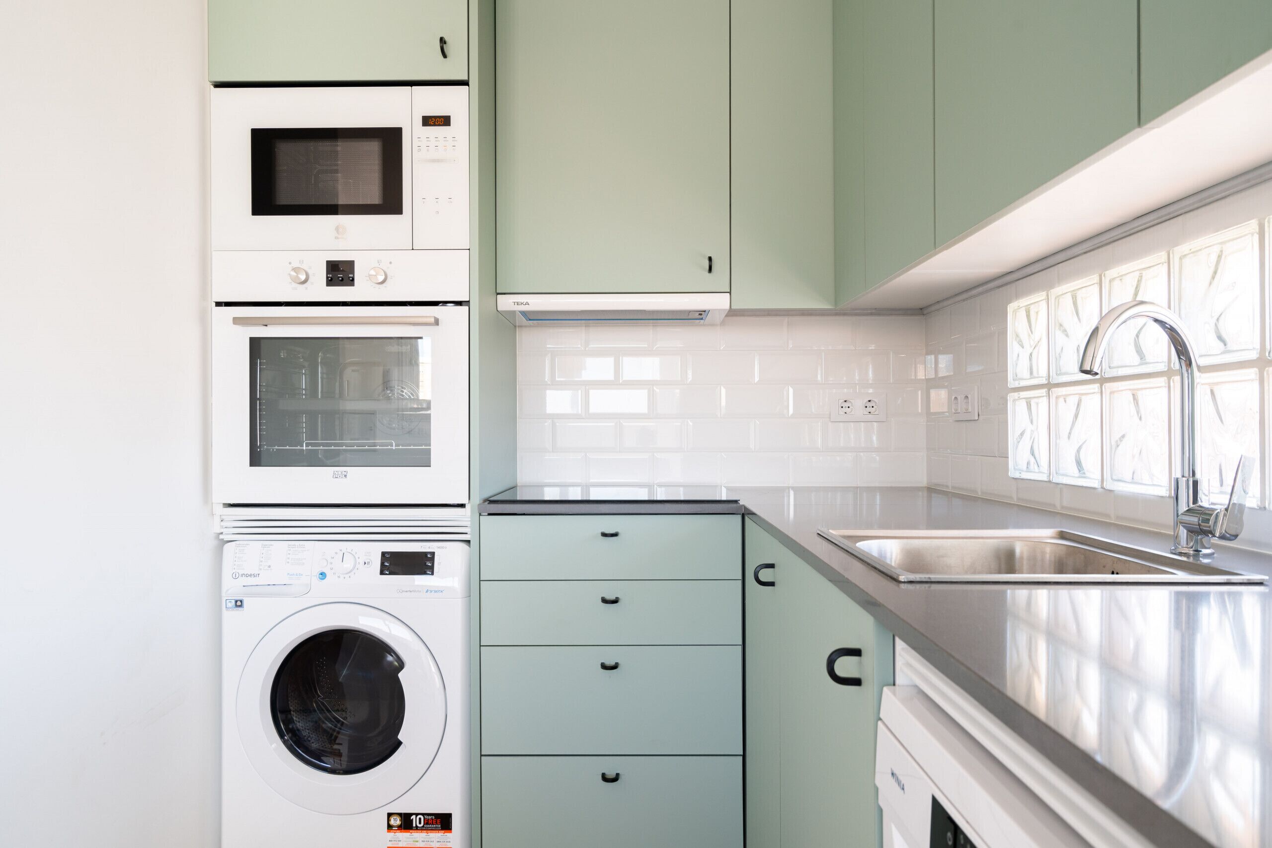 Une cuisine équipée d’un four encastré, d’un four à micro-ondes et d’un lave-linge, ainsi que d’un évier et de placards.