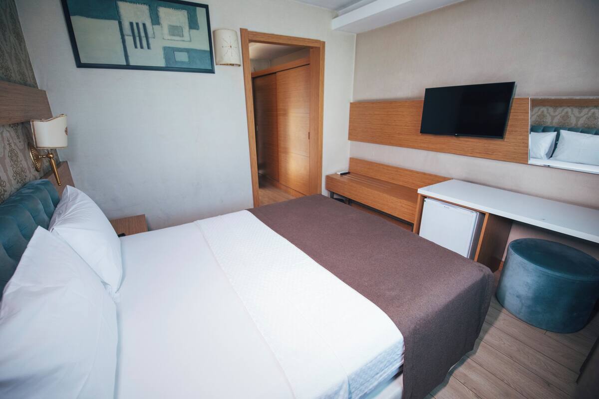 A hotel room with a bed, a desk, a television, and a wardrobe.