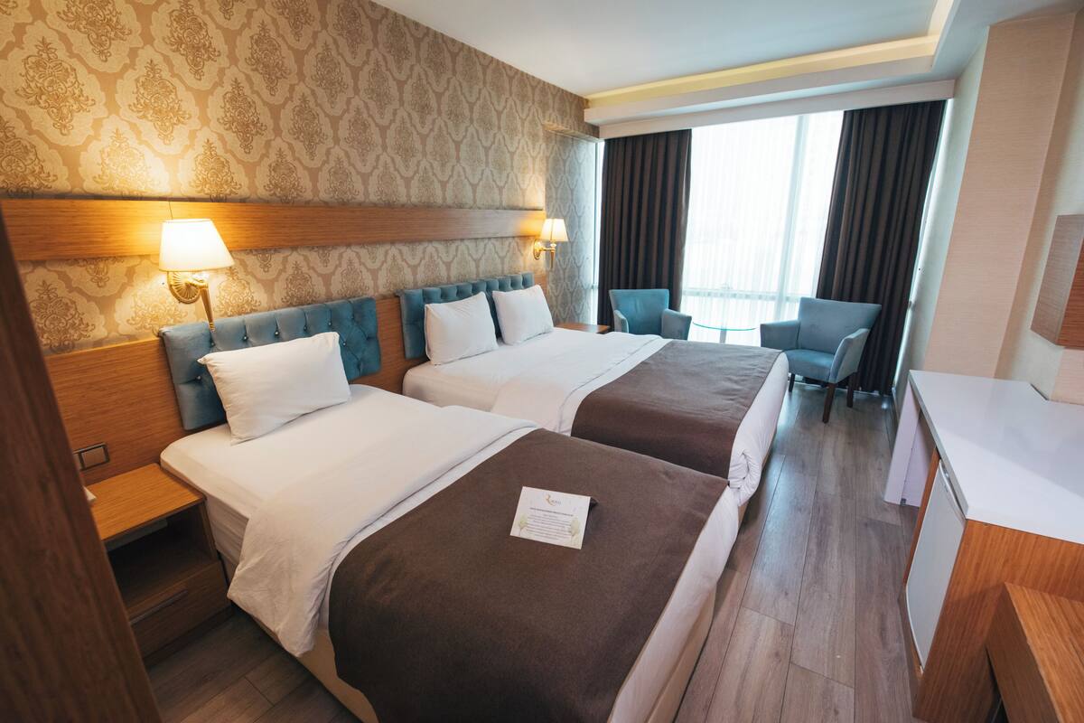 A hotel room with two beds, a desk, a chair, and a view of the outdoors.