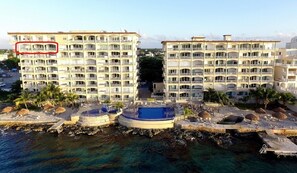 A hotel with multiple balconies, a pool area, and a view of the sea.