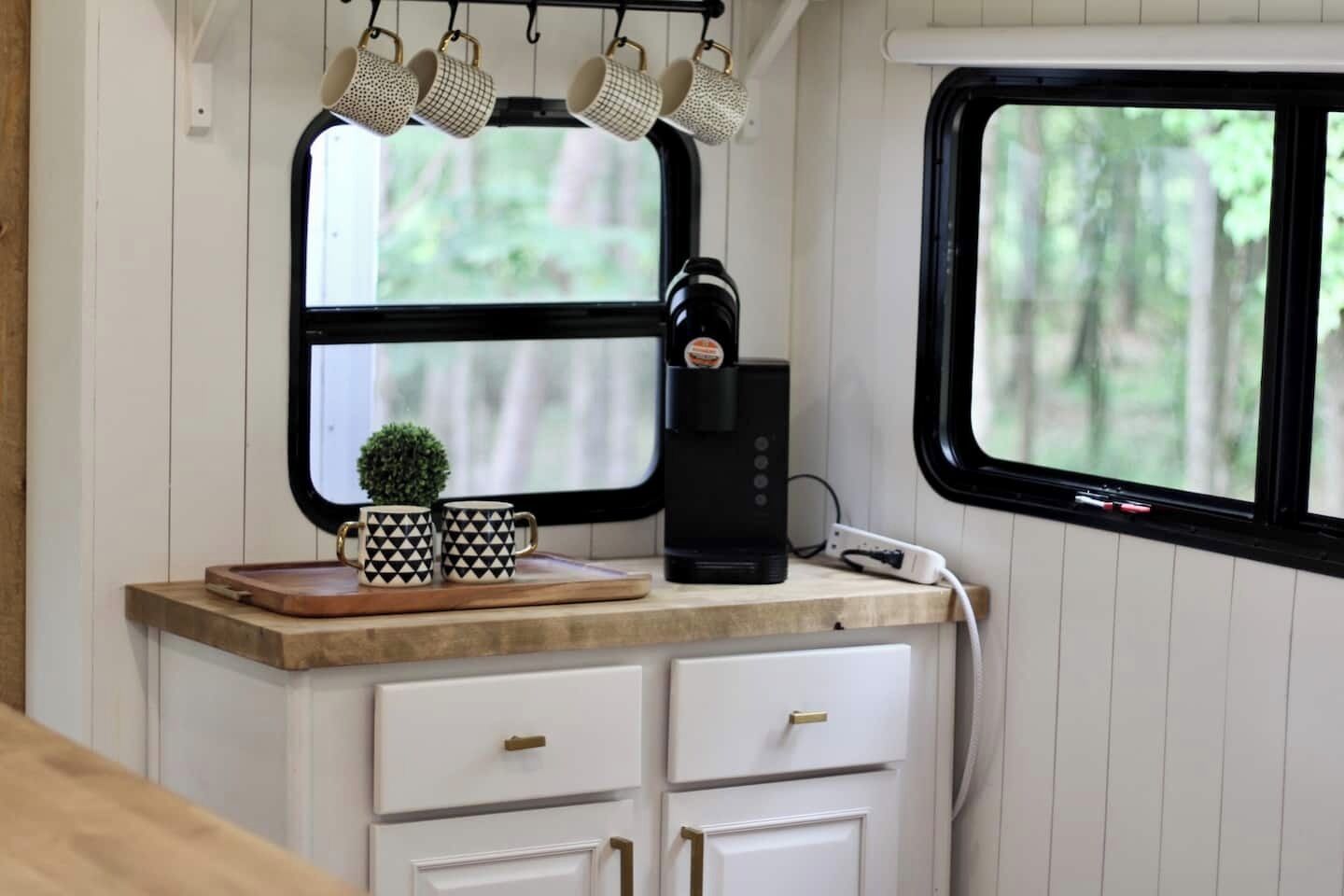 Une petite cuisine équipée d’une machine à café, de deux tasses et d’une petite plante en pot, le tout disposé sur un plateau en bois.