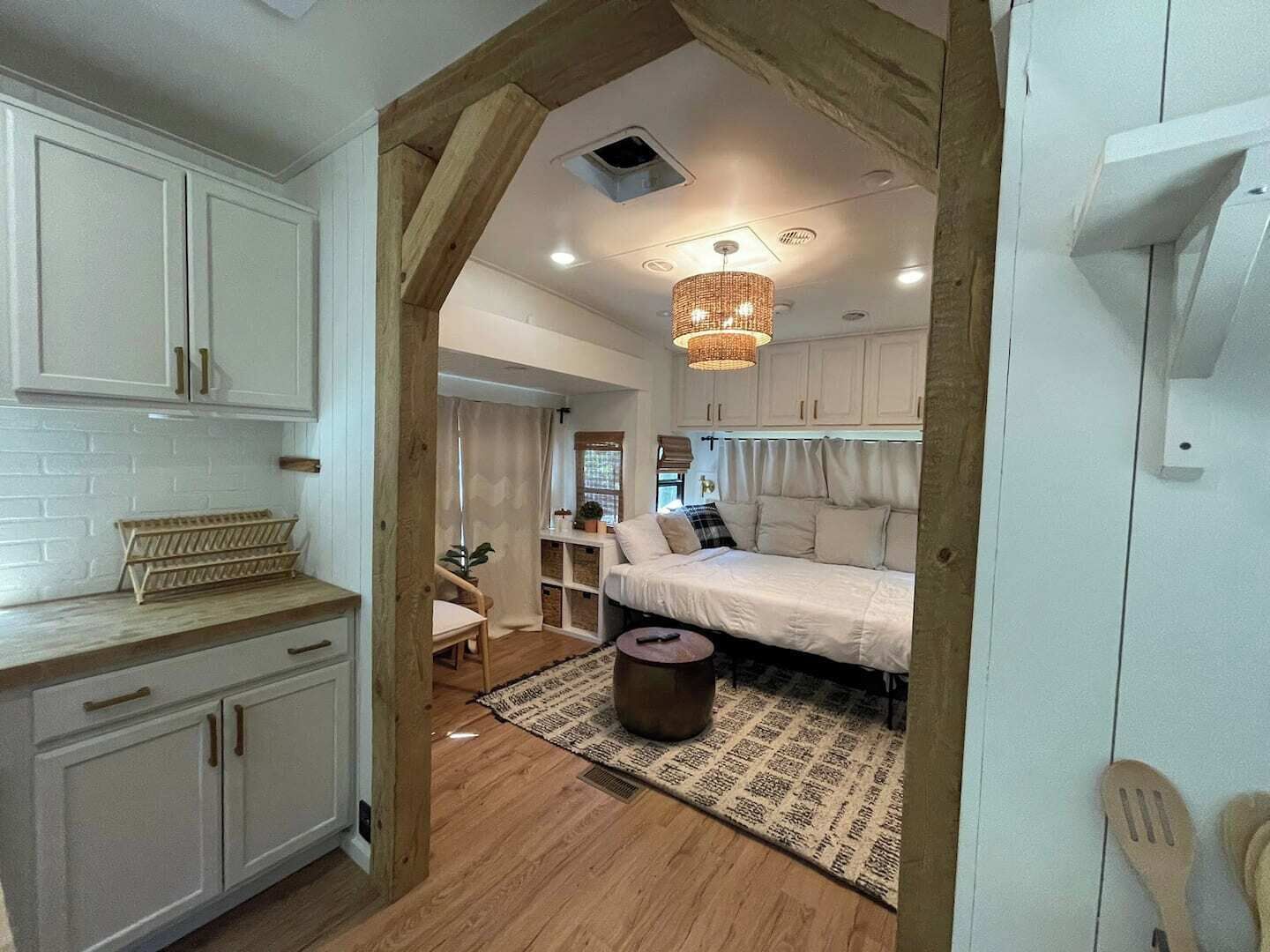 A compact, well-lit room with a bed, a small table, and a kitchen area with cabinets and a wooden counter.