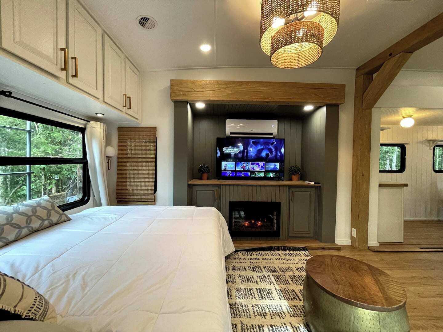 A bedroom with a large bed, a television mounted above a fireplace, and a window with curtains.