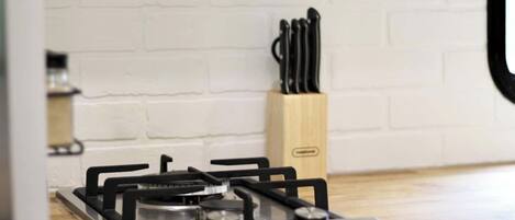 A kitchen with a gas stove, a knife block, and a white brick wall.