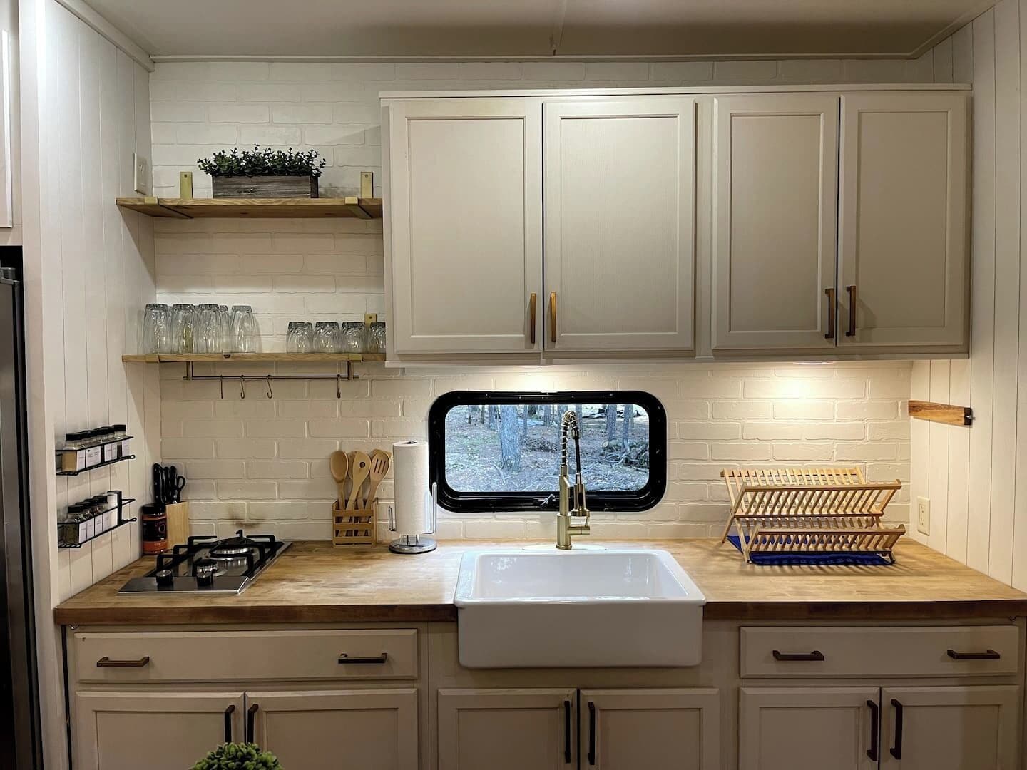 A kitchen with white cabinets, a wooden countertop, a window with a view, and a dish drying rack.