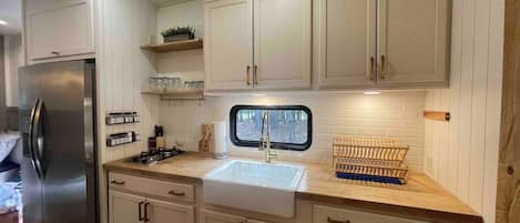 A modern kitchen with white cabinets, a stainless steel refrigerator, a window above the sink, and a wooden countertop.