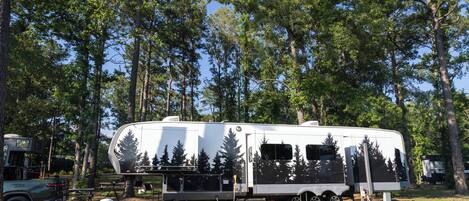 Una vehículo recreativo (RV) estacionado en un área boscosa, con árboles al fondo.