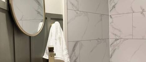Un bagno con parete rivestita in marmo, lavandino bianco con rubinetto dorato e mobile contenitore in legno.