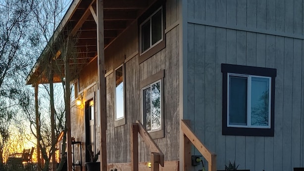 Une maison moderne en bois, dotée d’un porche, d’un escalier et d’une allée gravillonnée.