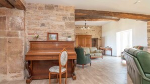 A spacious living room with a wooden piano, a green sofa, and a patterned armchair. - Le Grand Pressoir - Grande maison avec jardin (Nanton)