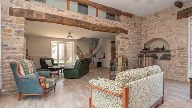 A spacious living area with a stone wall, wooden beams, and a green sofa. - Le Grand Pressoir - Grande maison avec jardin (Nanton)