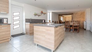 A modern kitchen with a central island, built-in appliances, and a dining area with wooden chairs. - Le Grand Pressoir - Grande maison avec jardin (Nanton)