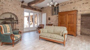 A rustic room with exposed stone walls, a wooden ceiling, a sofa, a chair, a cabinet, and a fireplace. - Le Grand Pressoir - Grande maison avec jardin (Nanton)