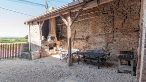 A rustic outdoor dining area with a stone wall, wooden beams, and a brick oven. - Le Grand Pressoir - Grande maison avec jardin (Nanton)