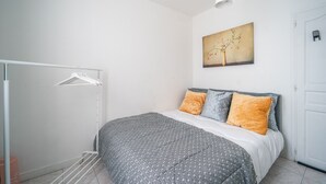 A bedroom with a bed, a hanging clothes rack, a painting, and a door. - L'Évasion Aulnaysienne - Appt pour 4 (Aulnay-sous-Bois)