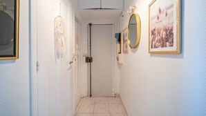 A narrow hallway with a white door at the end, a ceiling-mounted air conditioning unit, and framed pictures on the walls. - L'Évasion Aulnaysienne - Appt pour 4 (Aulnay-sous-Bois)