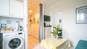 A compact kitchen with a washing machine, a table with a tablecloth, and a radiator. - L'Évasion Aulnaysienne - Appt pour 4 (Aulnay-sous-Bois)