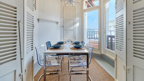 Un coin repas avec une table blanche dressée pour six personnes, des chaises transparentes et un lustre.