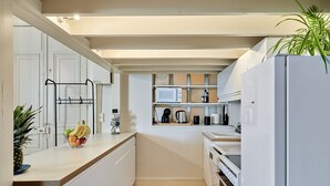 Une cuisine moderne avec des meubles blancs, un parquet en bois disposé en chevrons, un four à micro-ondes, une machine à café et un réfrigérateur.