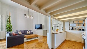 Un salon spacieux doté d’un parquet en bois à motifs de chevrons, d’un canapé gris, d’une table basse et d’un téléviseur.