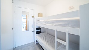 Een slaapkamer met stapelbed, een deur, een klein raam en een wandlamp.