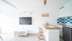 Een moderne keuken met een flatscreen televisie, houten barstoelen, een klein eiland en een inbouwoven.