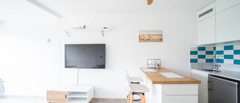 Una cocina moderna con televisor de pantalla plana, taburetes de madera, una pequeña isla y horno empotrado.