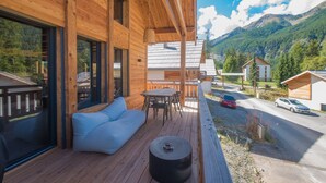 A wooden deck with a sofa and table, overlooking a road and mountains.