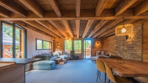 A spacious living area with a wooden ceiling, stone wall, and large windows.